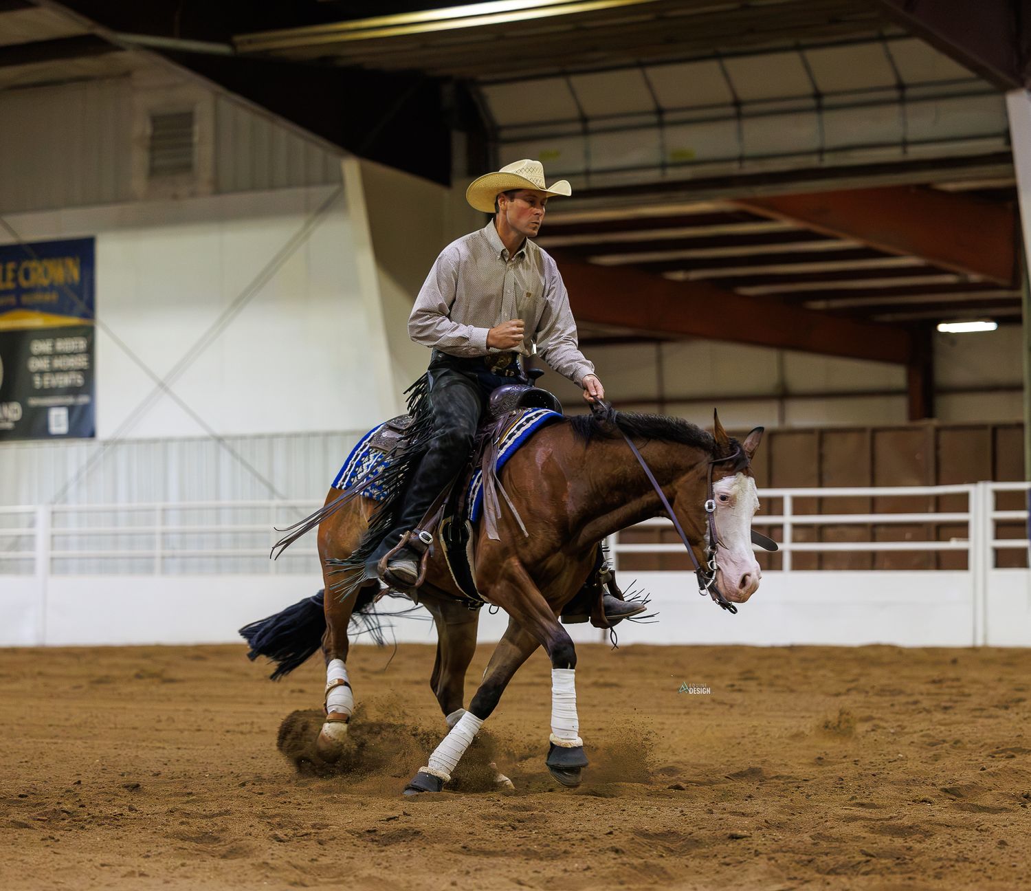 Cowboy riding a bay horse performing reining maneuver in indoor arena during equestrian competition.