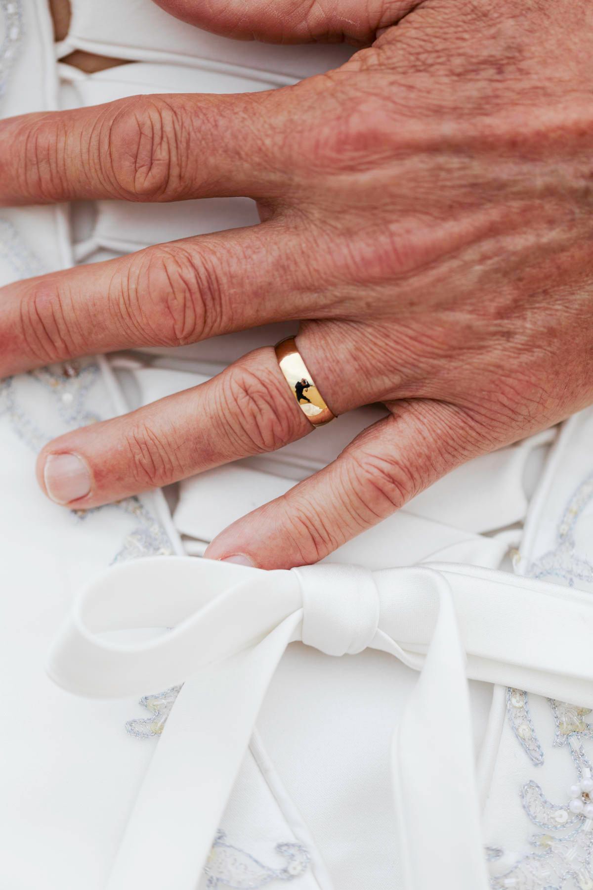 Close-up sequence of hands removing a gold wedding ring from a finger against white fabric background.