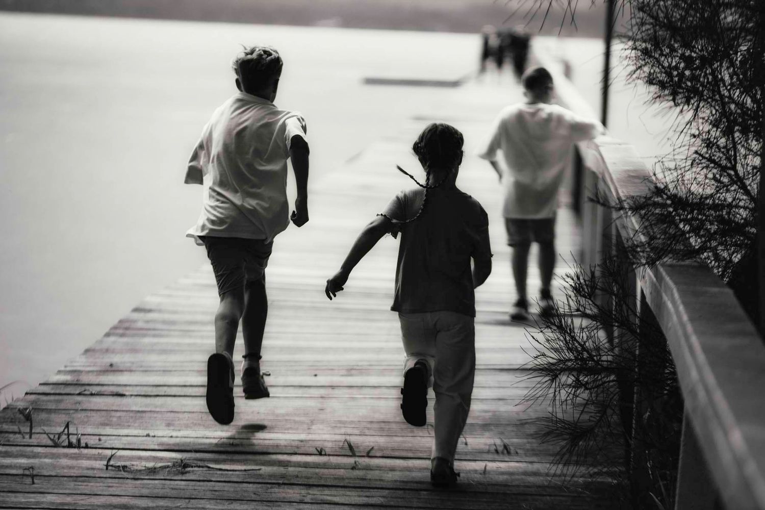 Black and white photo of three people running together on a wooden boardwalk or dock.