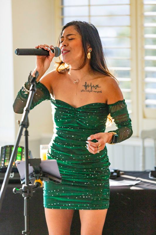 A performer in a sparkly green dress sings on stage with a microphone.