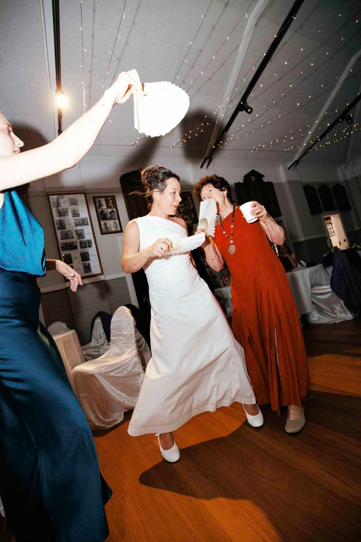 Wedding guests dancing together at a reception under twinkling lights on a wooden dance floor.