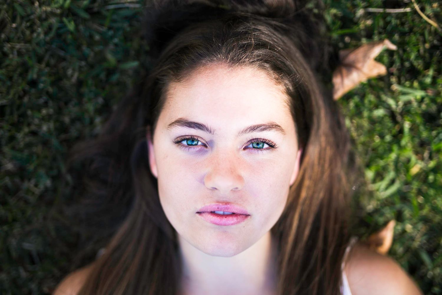 Close up portrait of a person with long brown hair and bright eyes against a natural green background.