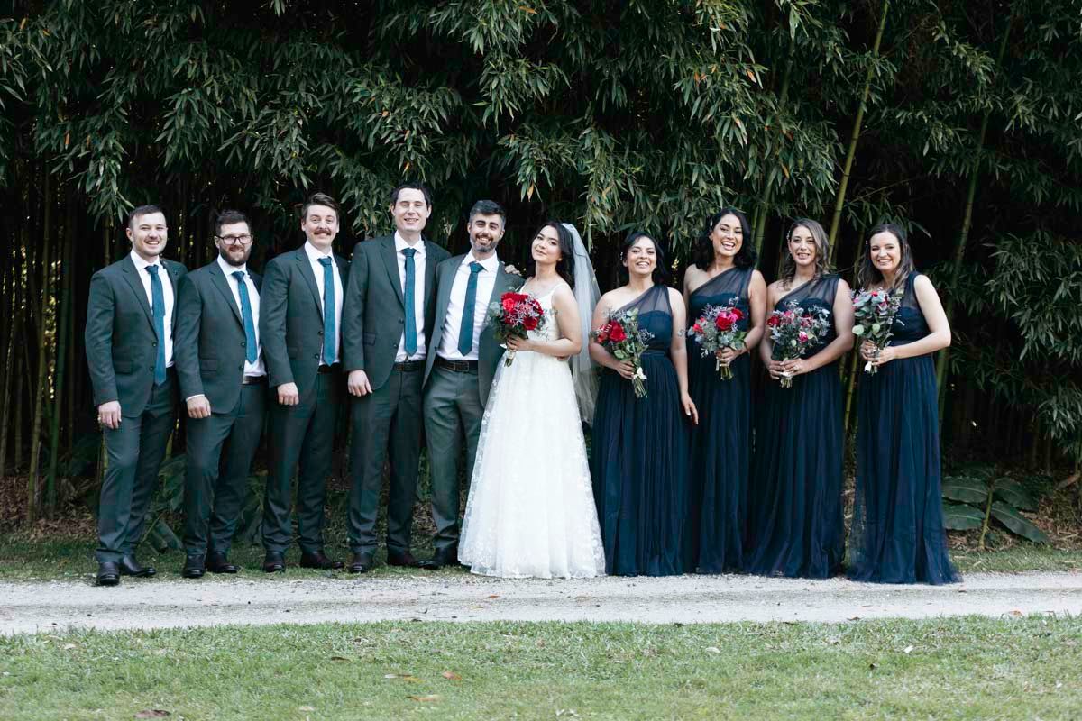 Wedding party in navy and white attire posed outdoors for formal group photos.
