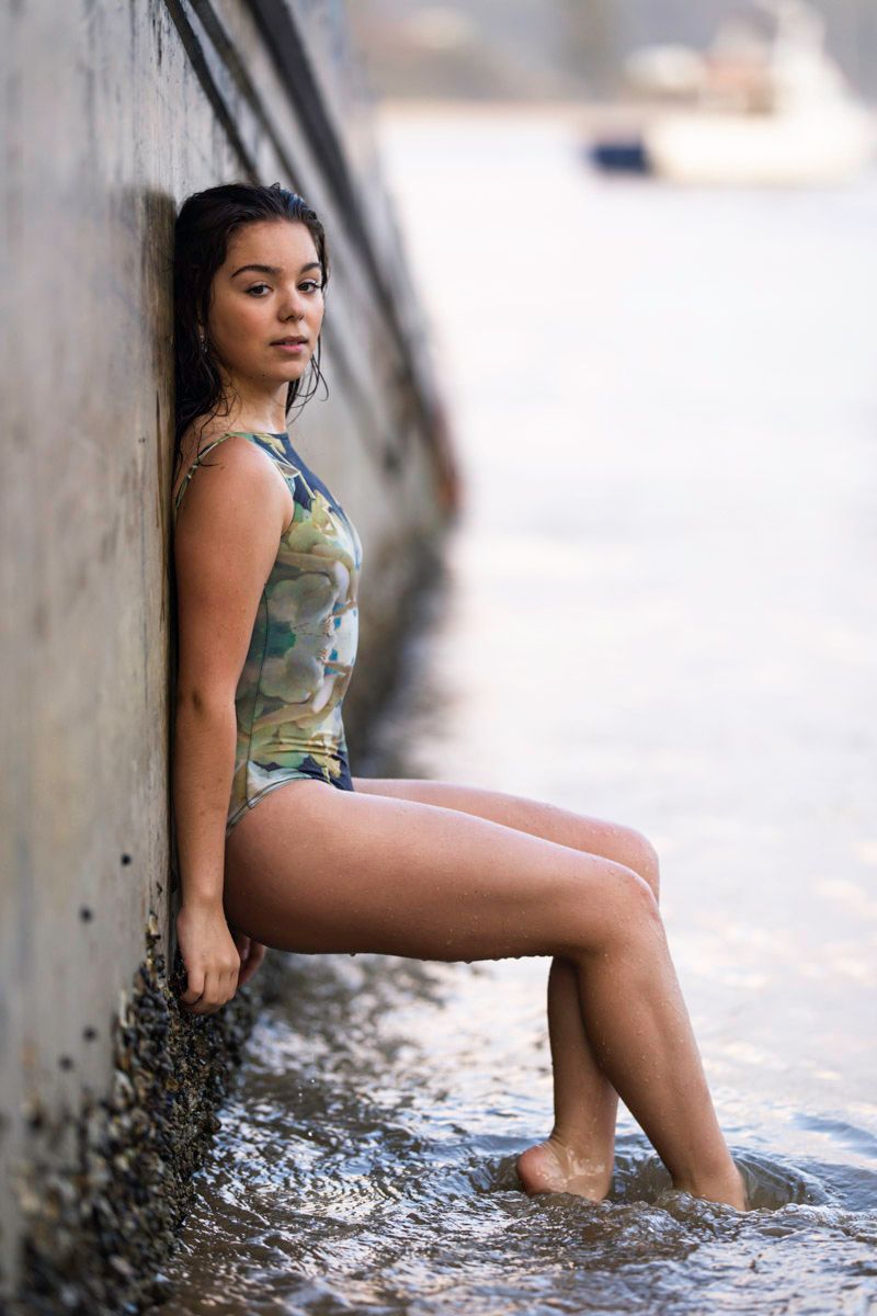 A woman in a camouflage swimsuit poses in shallow water against a concrete wall.
