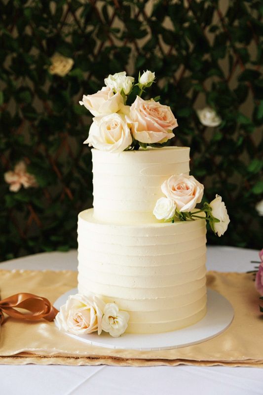 An elegant white wedding cake decorated with fresh peach roses on a white plate.