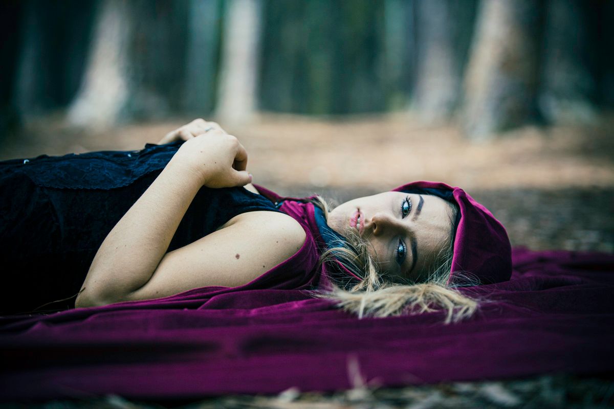 A person in a purple dress lies on a wooden surface in a moody outdoor setting with dramatic lighting.