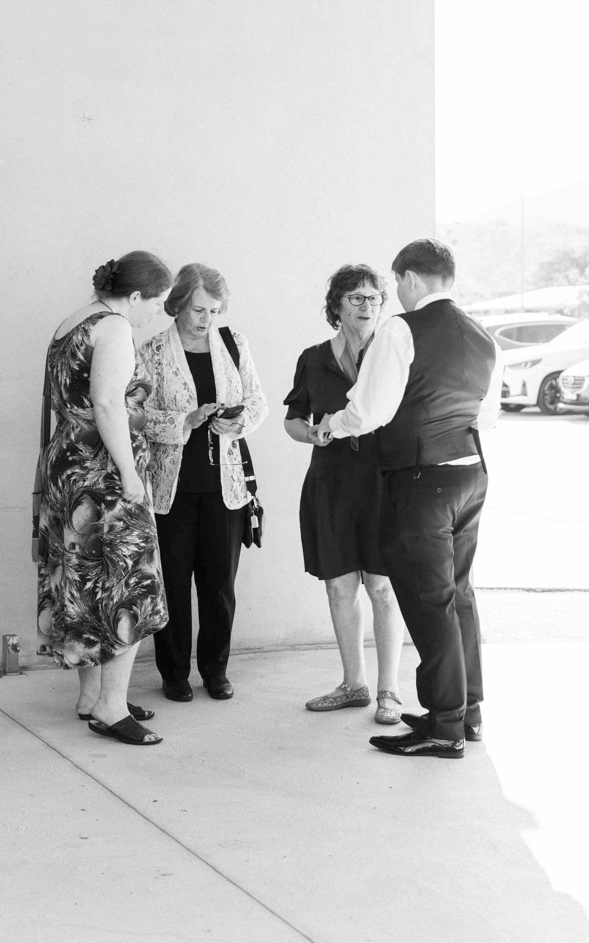 A line of people bent over looking down at something on the ground in a white hallway or corridor.