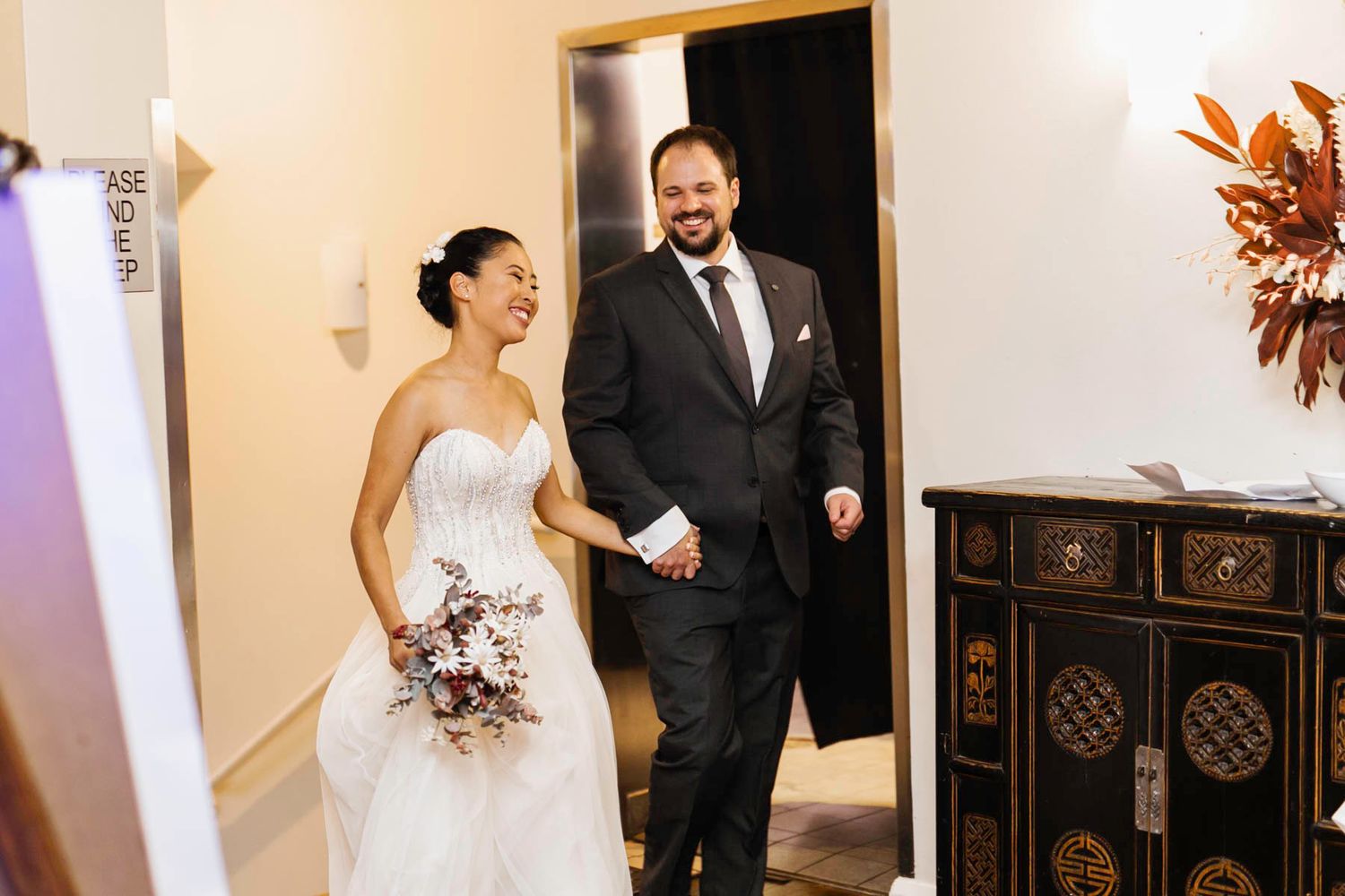 A bride and groom share a joyful moment together in a brightly lit hallway during their wedding celebration.