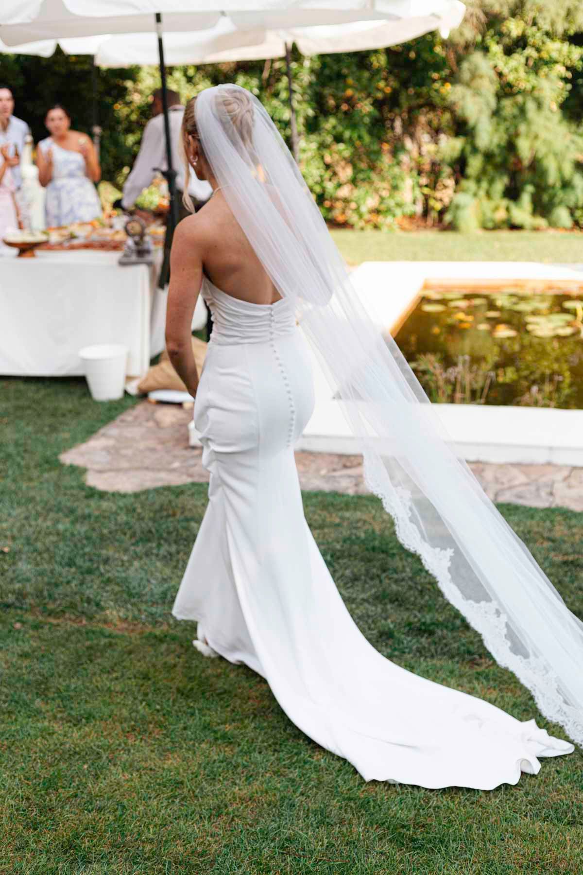 Close-up sequence of a flowing white wedding dress train trailing on green grass during an outdoor ceremony.