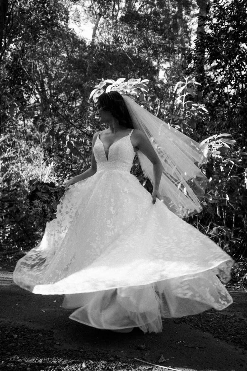 Bride in a voluminous white gown spinning gracefully in a wooded outdoor setting.