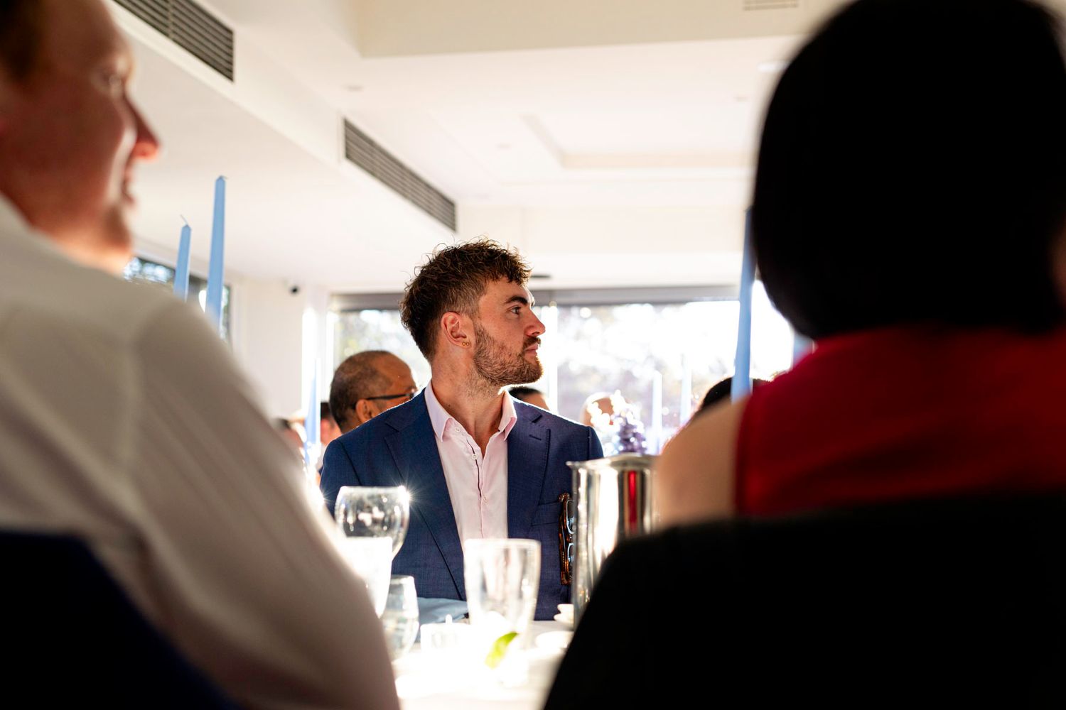 A person in a blue suit jacket laughs while speaking to others during a social gathering indoors.