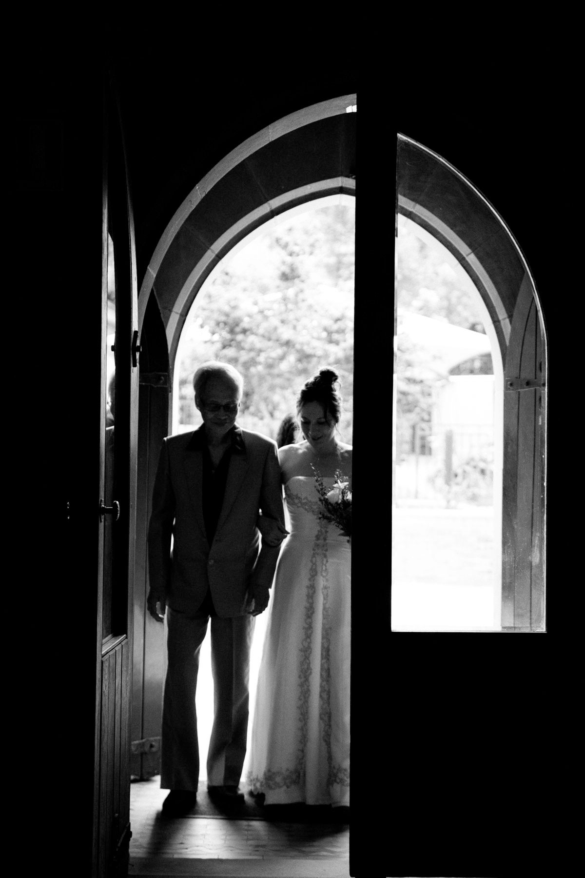A silhouetted couple stands in an arched doorway of a church in black and white photography.