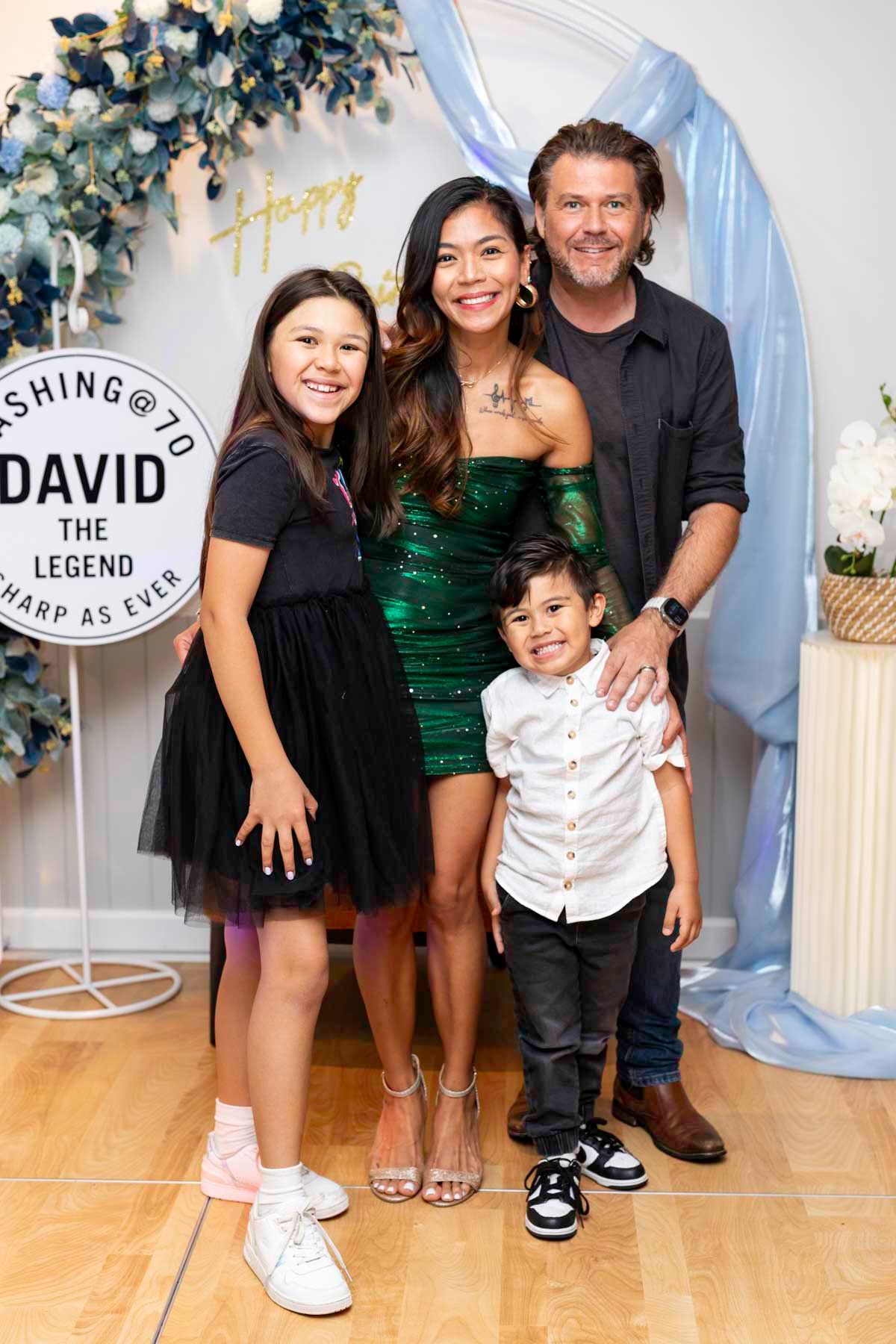 A family poses together at a celebration with blue and gold decorations against a light backdrop.