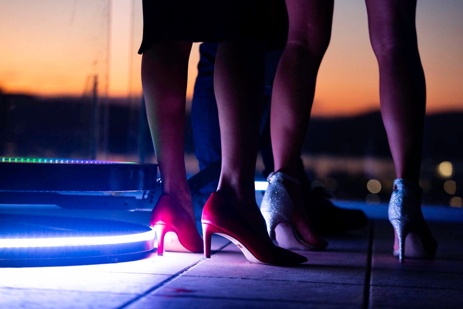 Silhouetted feet of dancers on a glowing dance floor with blue and purple lighting effects at night.