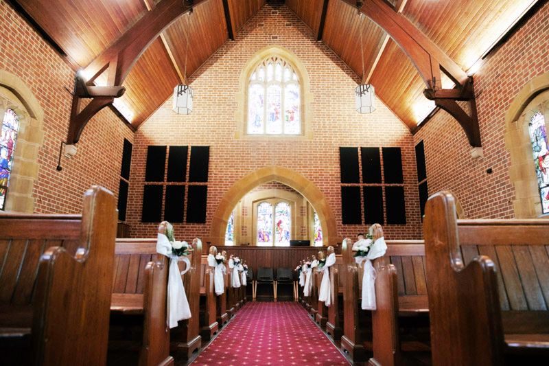 Interior of a church with wooden beams and stained glass windows along red carpeted aisle.