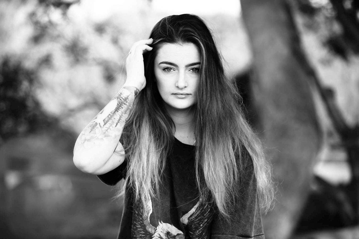 Black and white portrait of a woman with long dark hair wearing a black top in an outdoor setting.