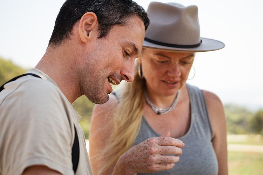 A couple shares intimate moments outdoors while wearing casual clothing and a sun hat in natural lighting.