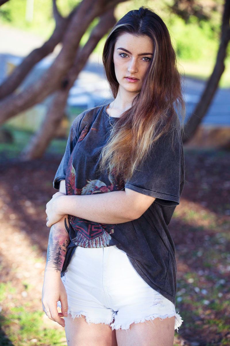 Person in a black t-shirt and distressed white denim shorts poses outdoors in natural lighting.