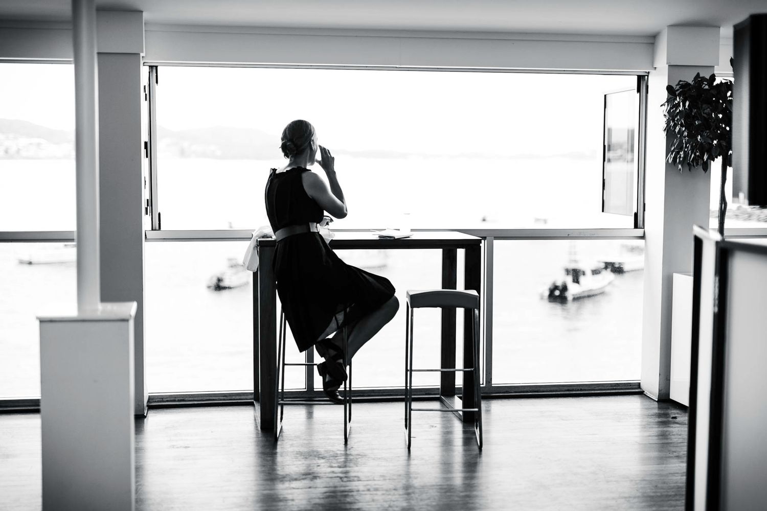A black and white panoramic view of a minimalist interior hallway with silhouetted figures by windows.