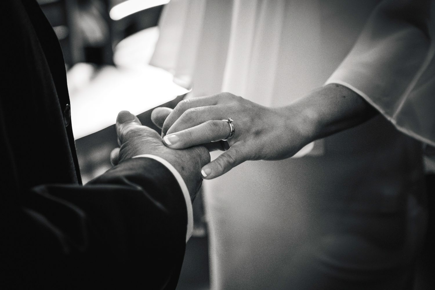 Close-up of hands in an intimate black and white wedding ceremony moment.