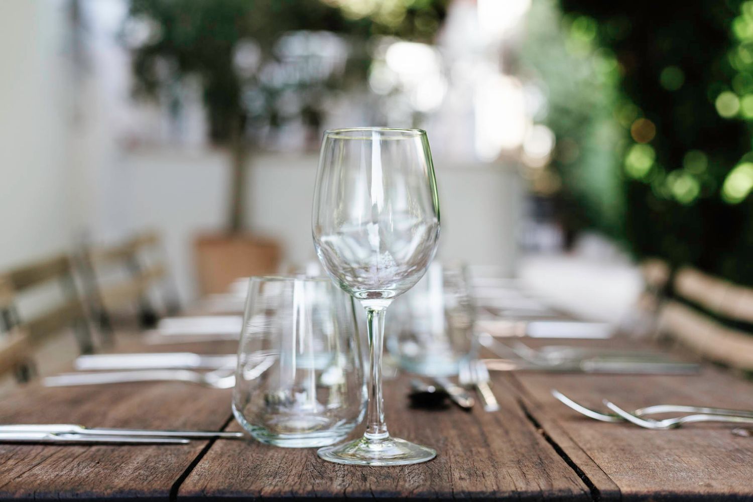 Empty wine glasses and place settings on a rustic wooden table set for outdoor dining.