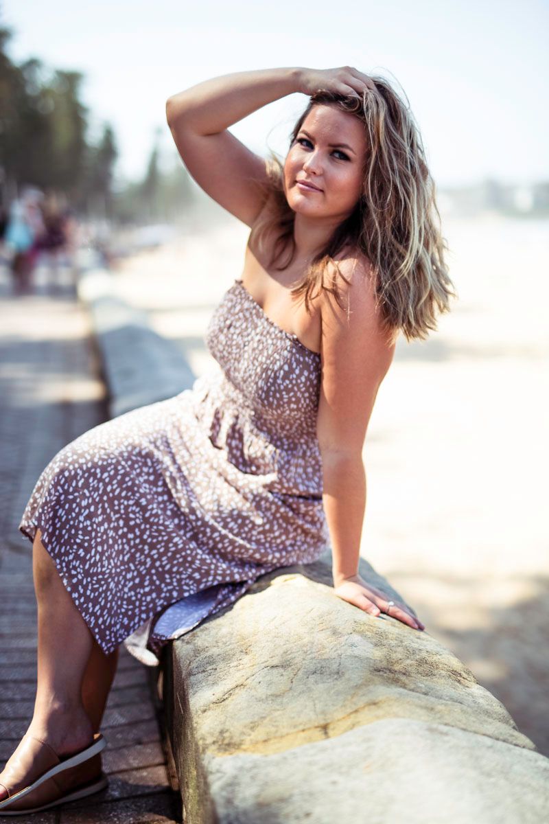 A woman in a leopard print dress poses on a large rock at a beach during golden hour.