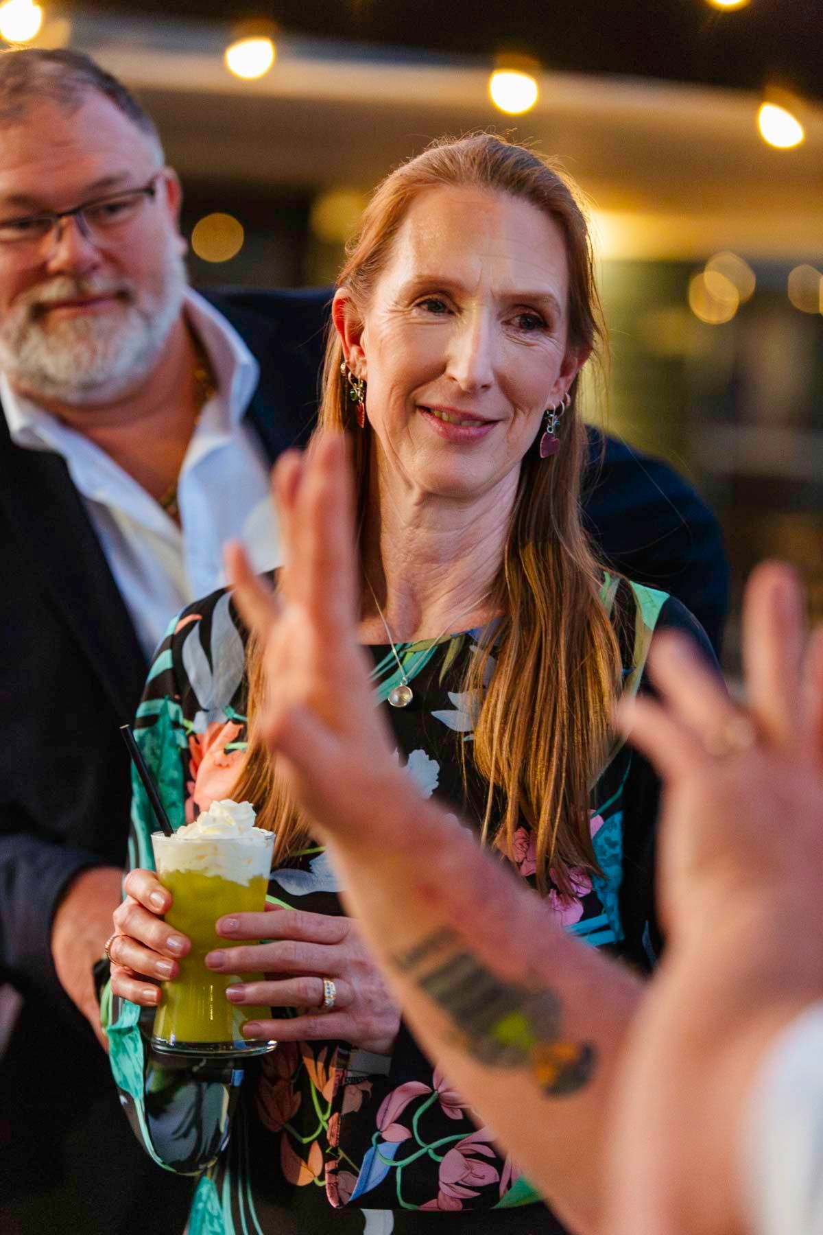 People enjoying colorful cocktails at a social gathering with ambient lighting in the background.