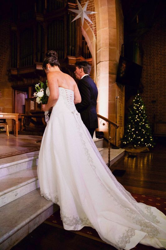 Elegant white wedding dress with lace detail and long train in a church setting.