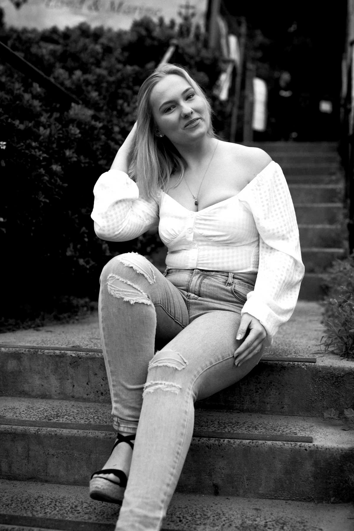 A person in light-colored clothing sits casually on concrete steps in a black and white artistic portrait series.