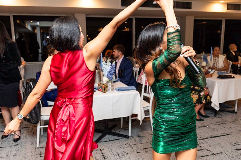 People dancing at a reception wearing festive red and green dresses.