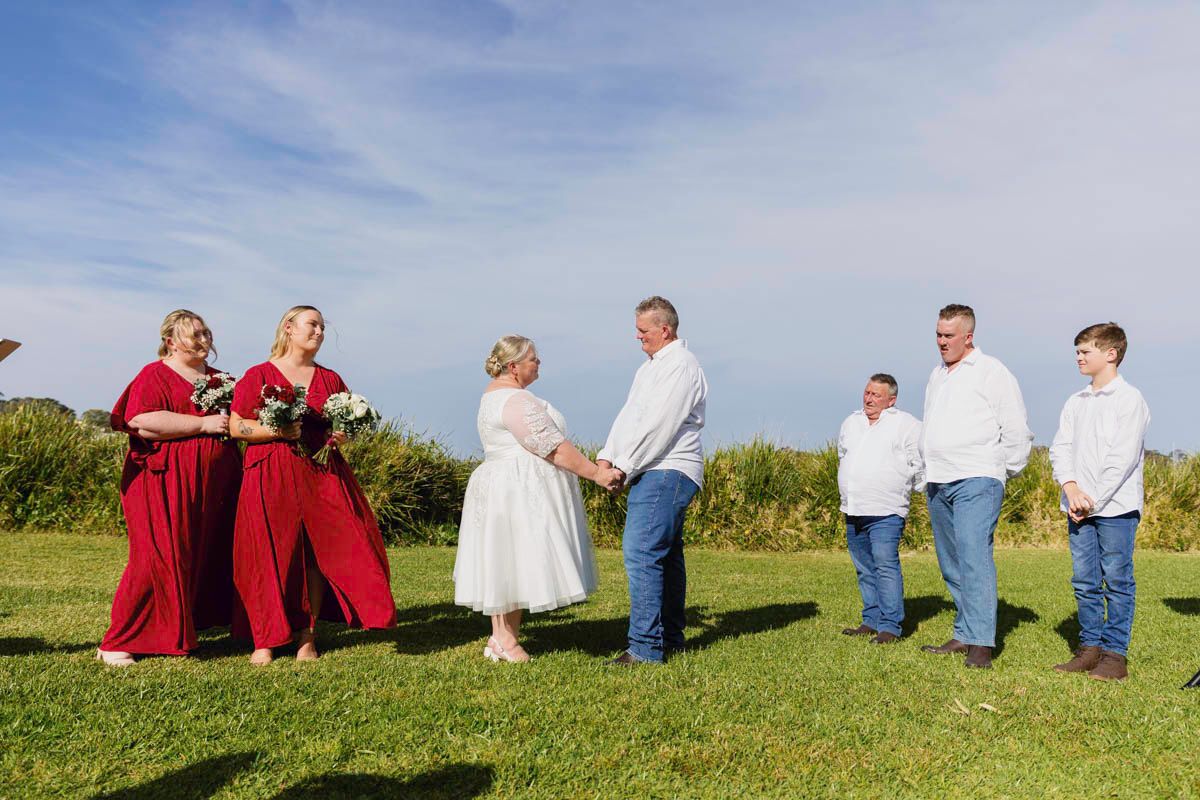 Family portrait session on a grassy hill against a bright blue sky.