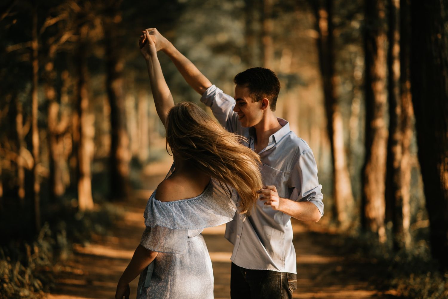 A couple dances together in a sunlit forest during golden hour, creating a romantic and ethereal atmosphere.