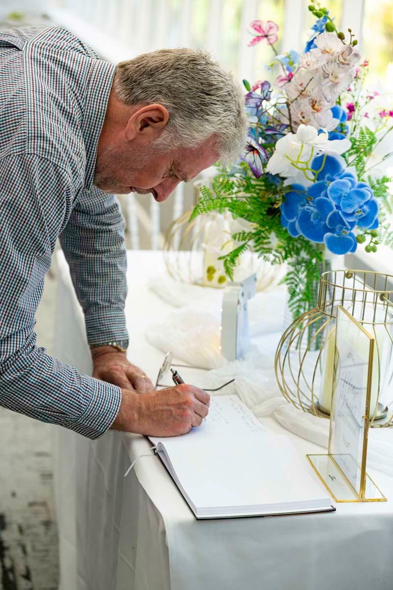 Person signing documents at a table decorated with blue and white floral arrangements.