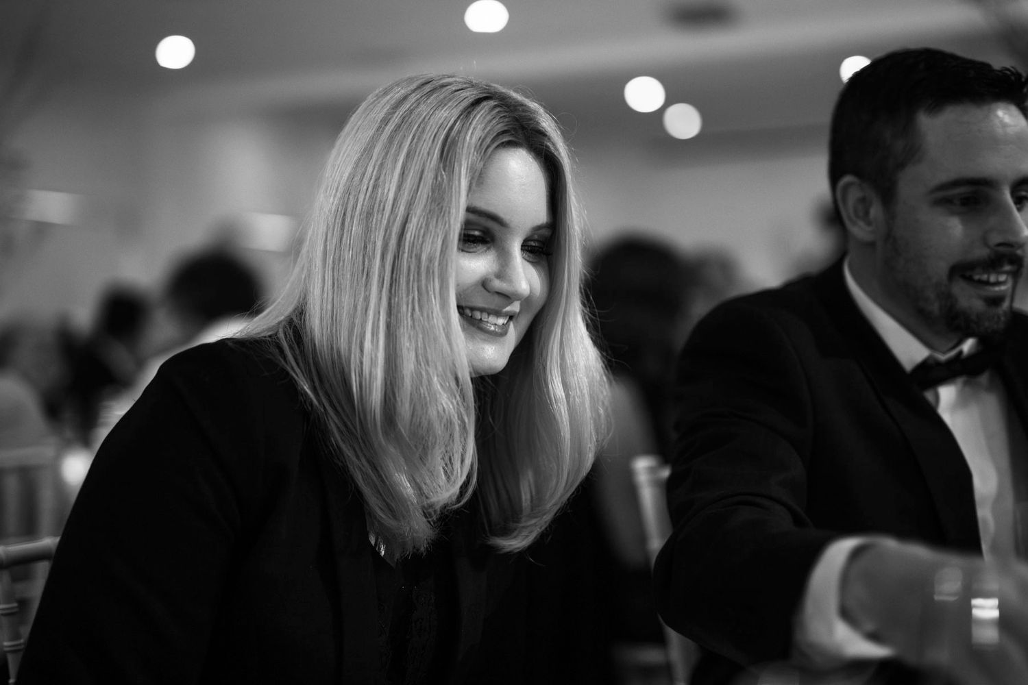 Black and white candid photo of people at a formal event with someone smiling in the foreground.