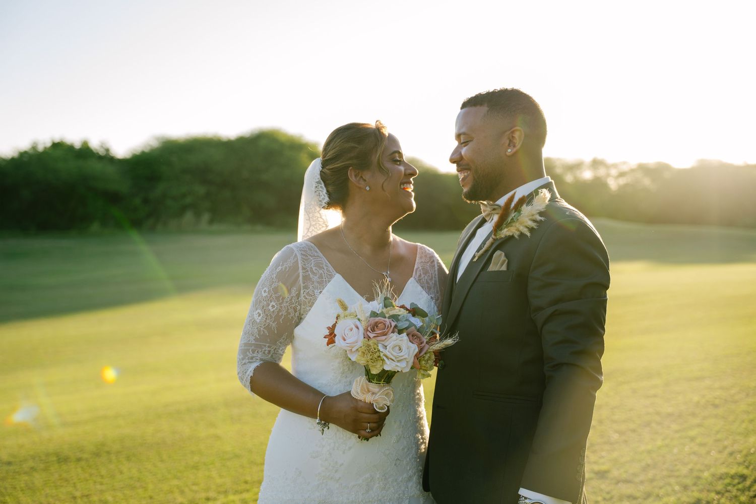 Bride and groom share a golden hour moment on lush green golf course lawn.