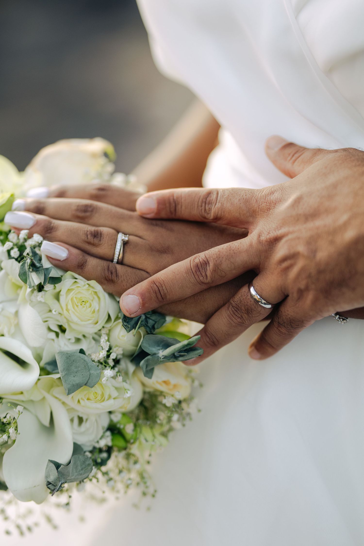 Newlyweds display matching silver wedding rings over elegant white rose bridal bouquet.