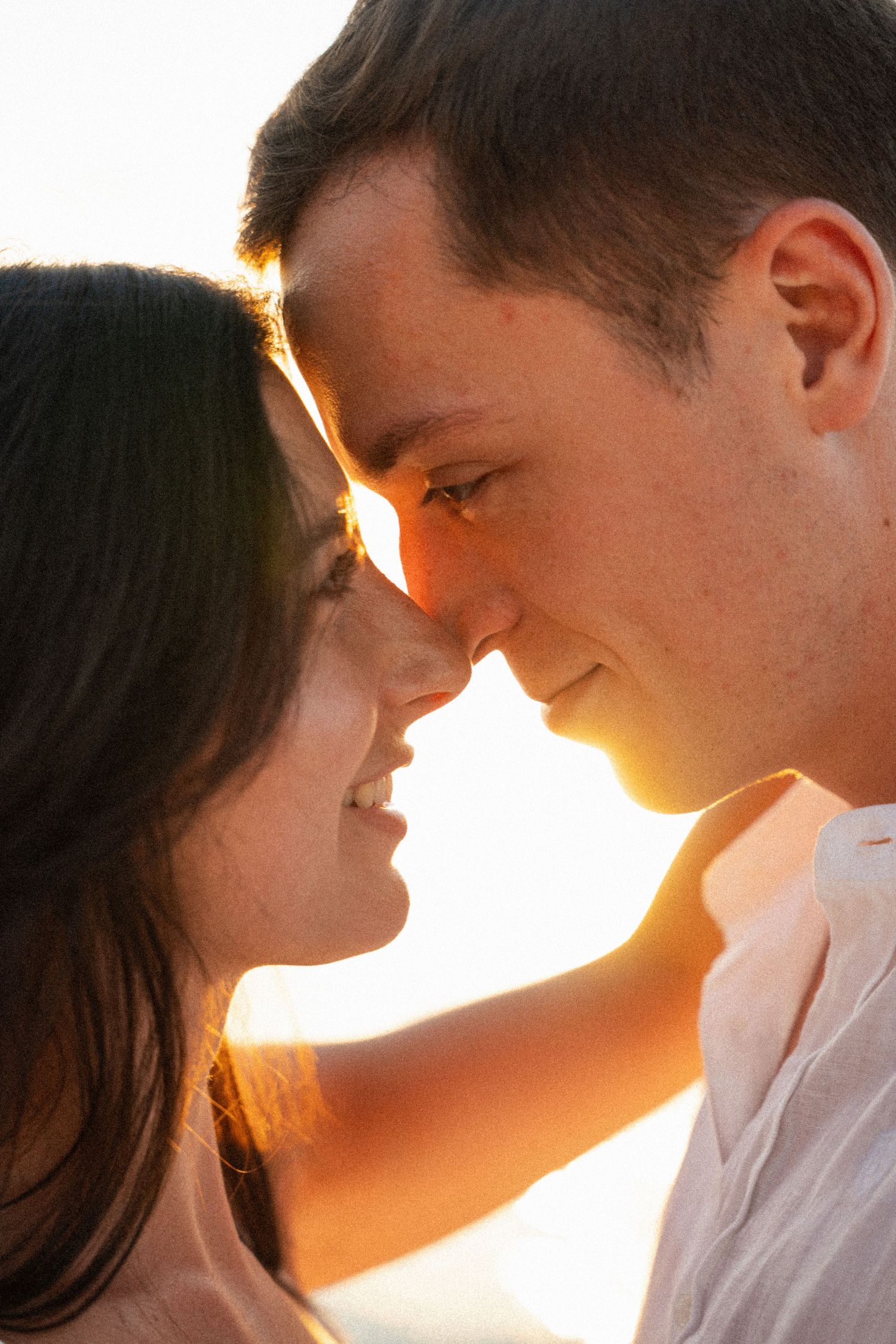 A couple shares a romantic moment at golden hour, touching foreheads and smiling softly in warm sunset light.