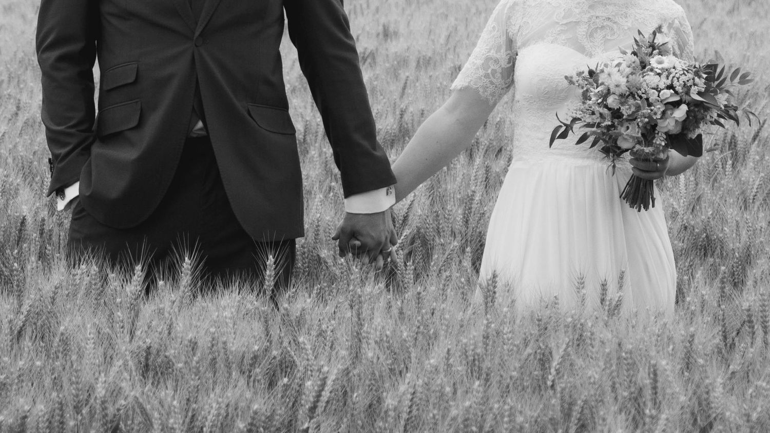 Lower half of bride and groom's body, holding hands in a field of what, captured in a natural lifestyle style by EvieSJPhotography.