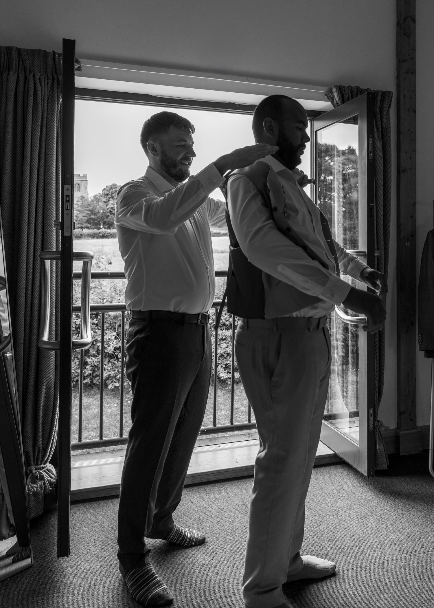 Jack helping Aaron with his waistcoat during morning prep at Rock Village Hall ahead of their wedding ceremony.