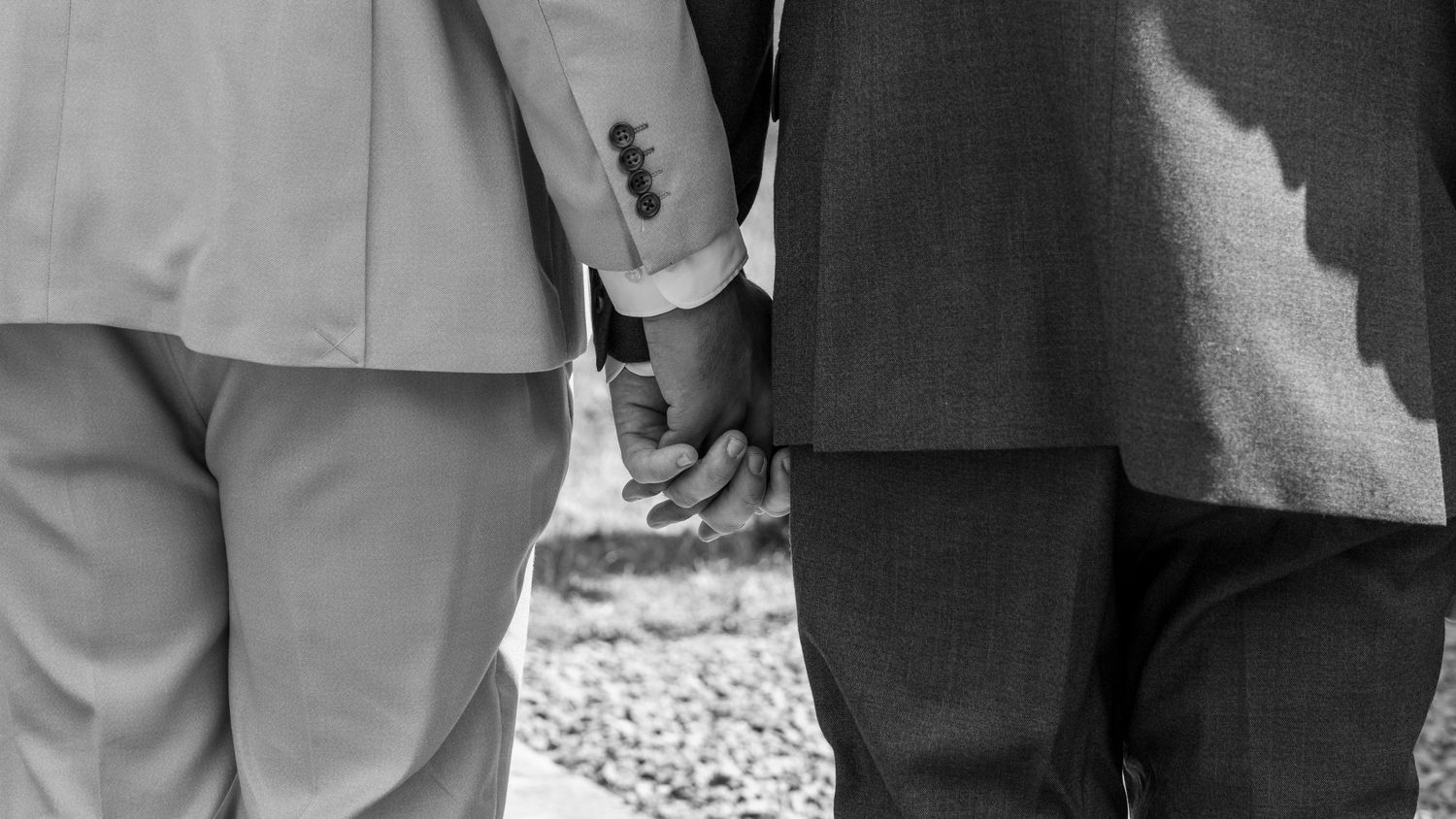 Two grooms holding hands in an emotional black-and-white photograph during their wedding day.