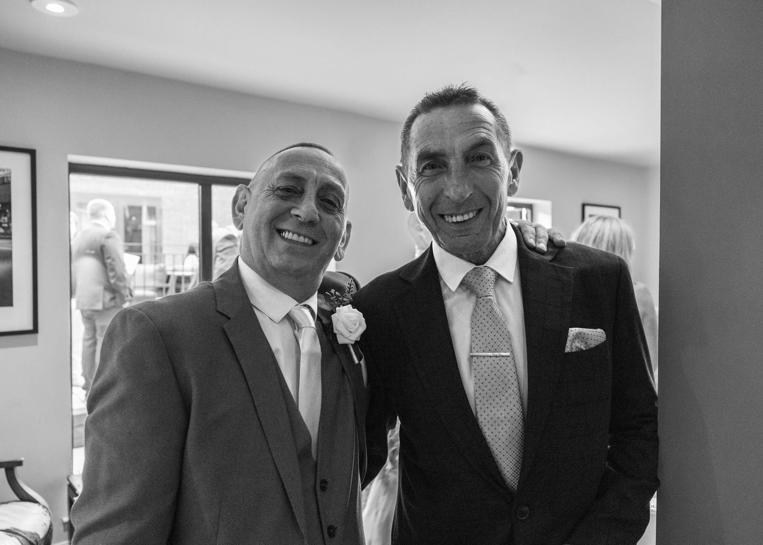 Two wedding guests smiling together in their suits during Cortney and Dan's wedding day.