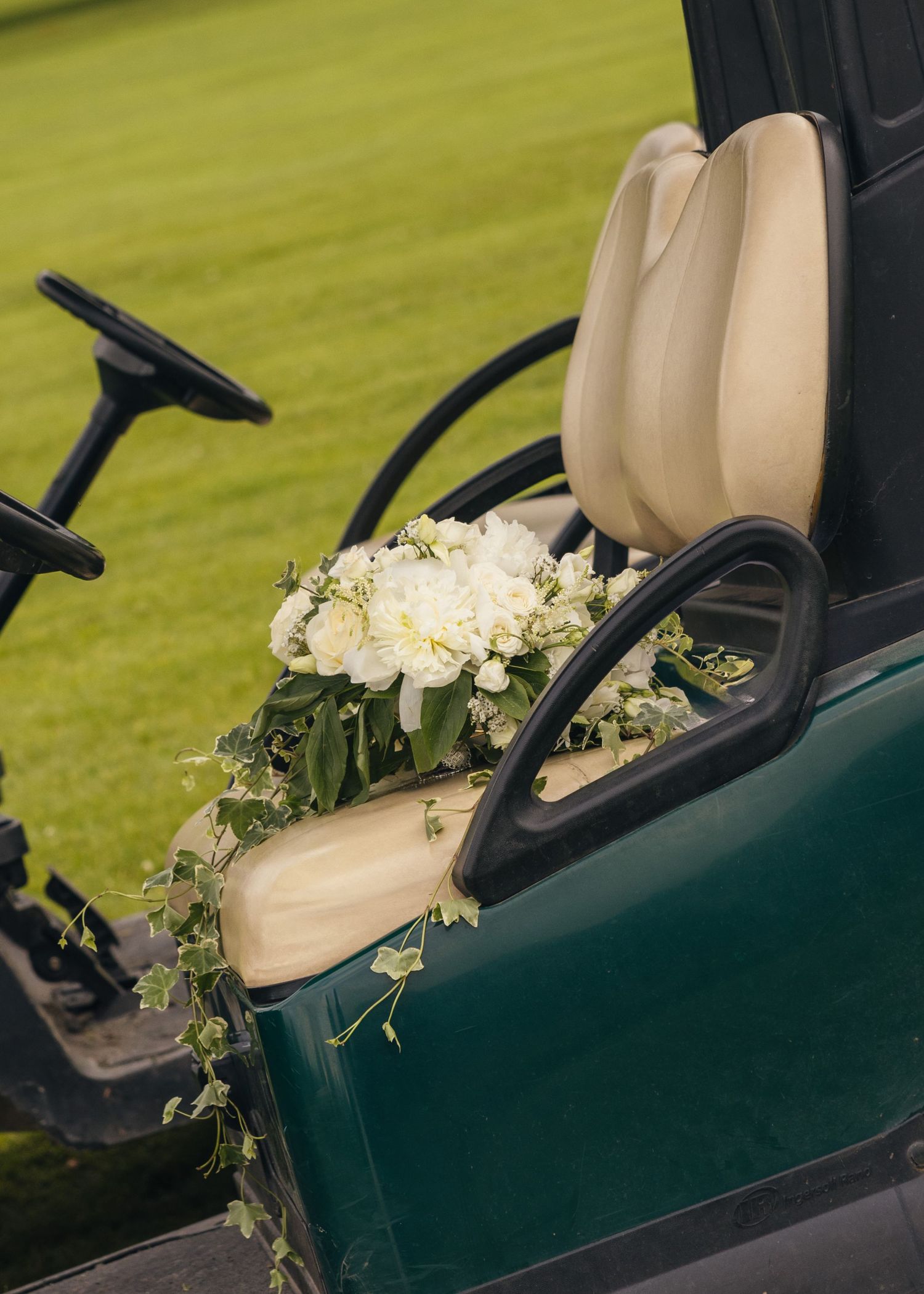 White bridal bouquet resting on the seat of a green golf cart at the wedding venue.