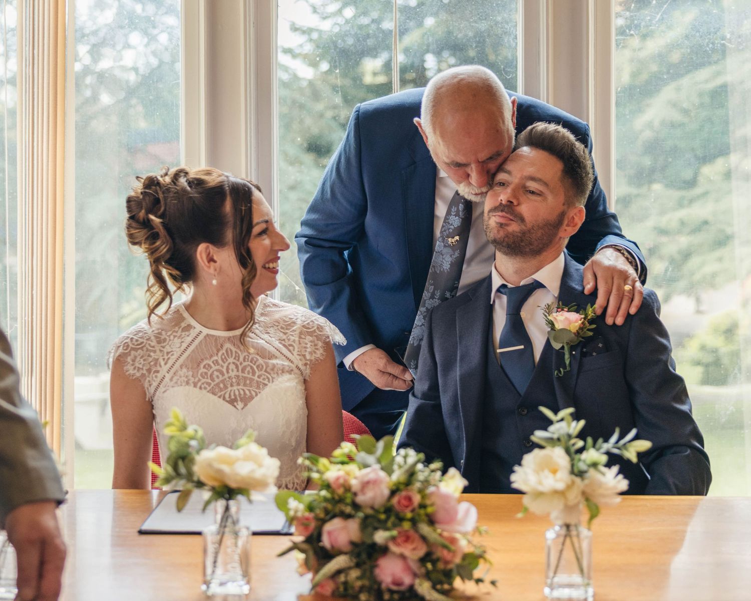 A bride and groom sharing a special moment with his father after the ceremony, captured by EvieSJPhotography.