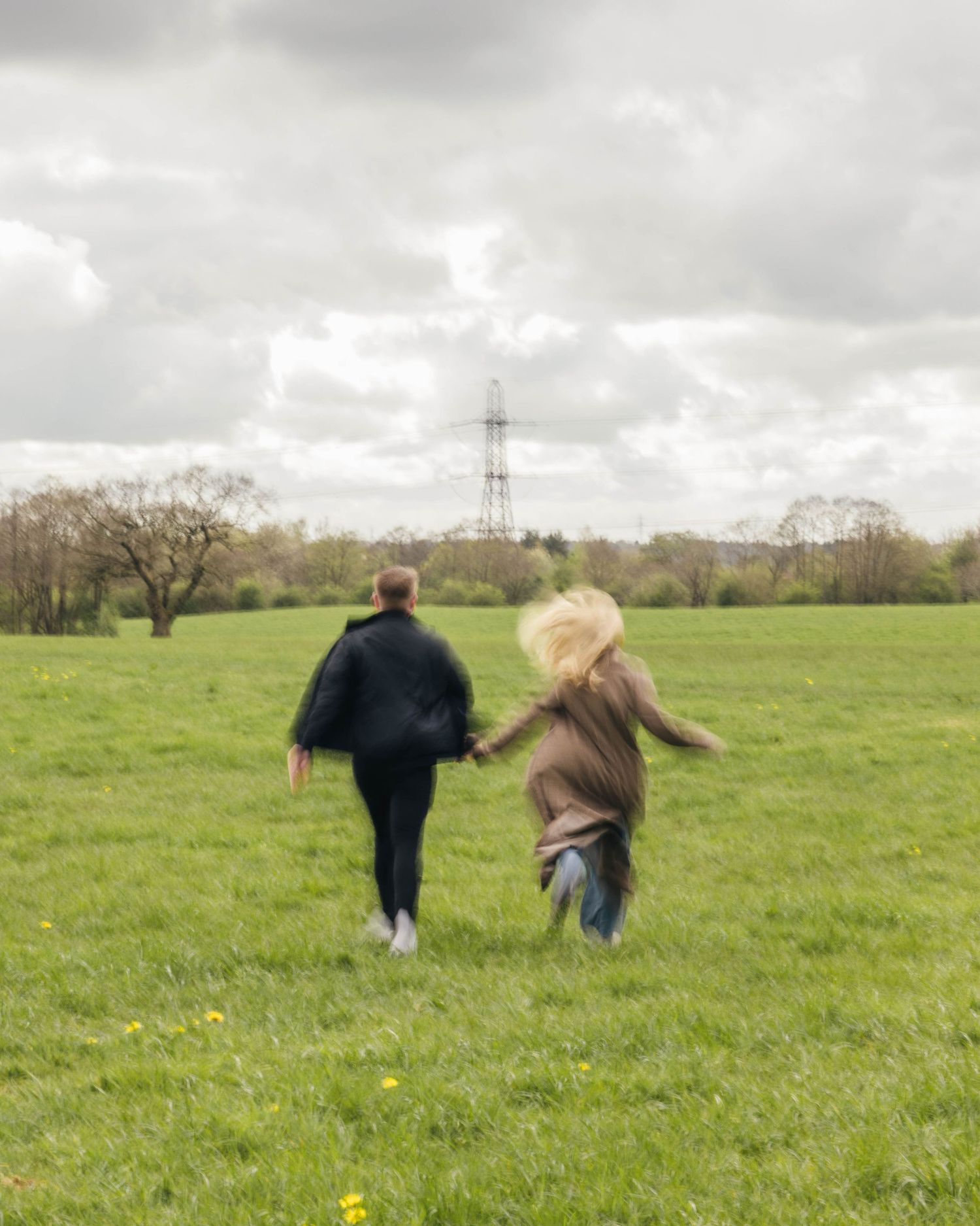 A couple having fun running together in a field during a photoshoot.