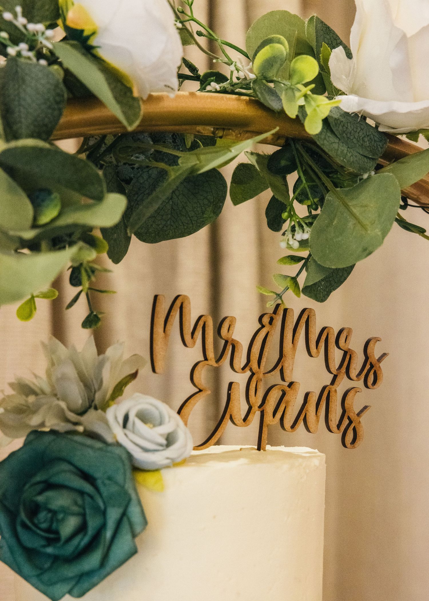 Close-up of a personalised Mr and Mrs Evans topper on a flower-decorated wedding cake.