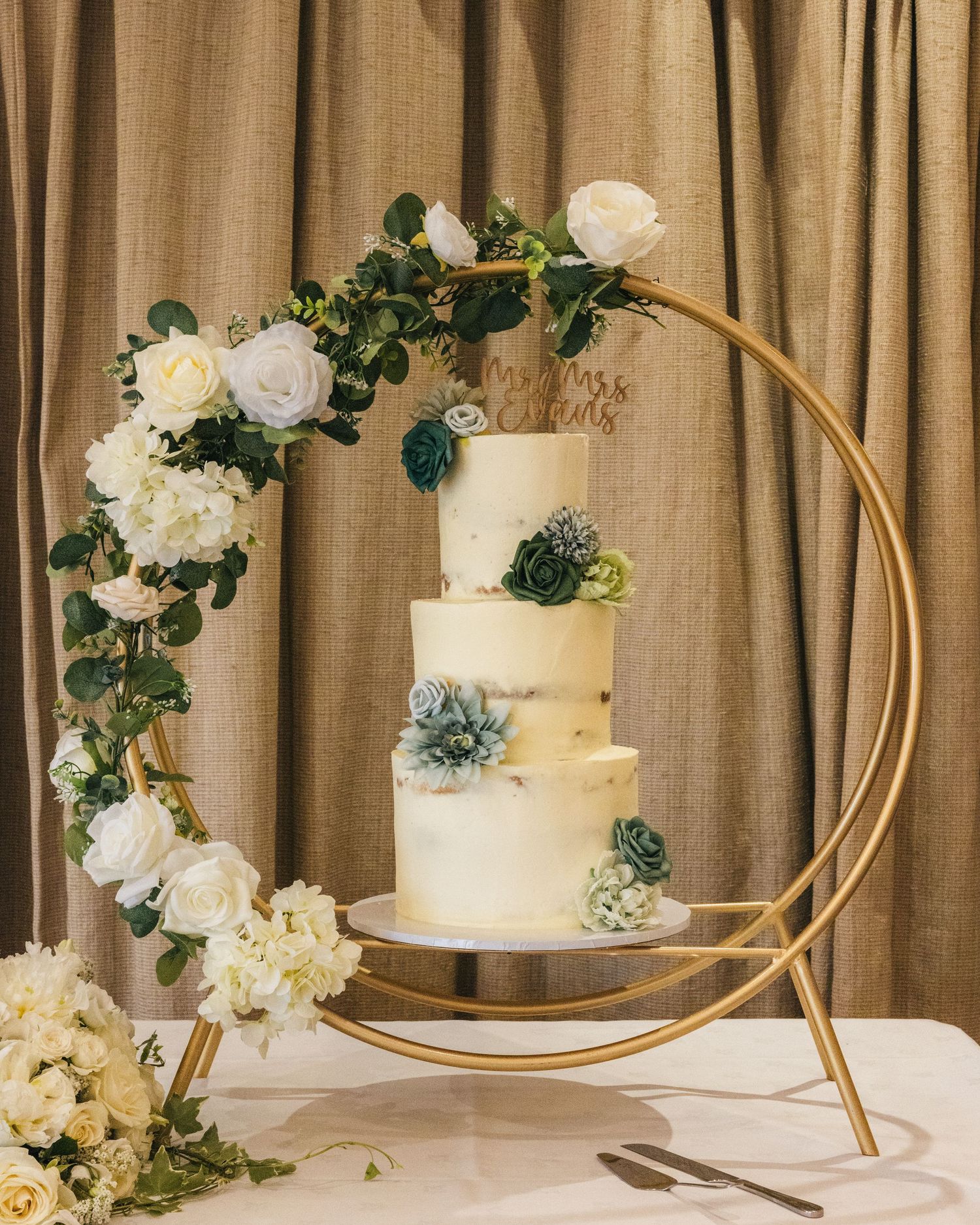 Three-tier wedding cake decorated with white and green flowers on a gold circular stand.