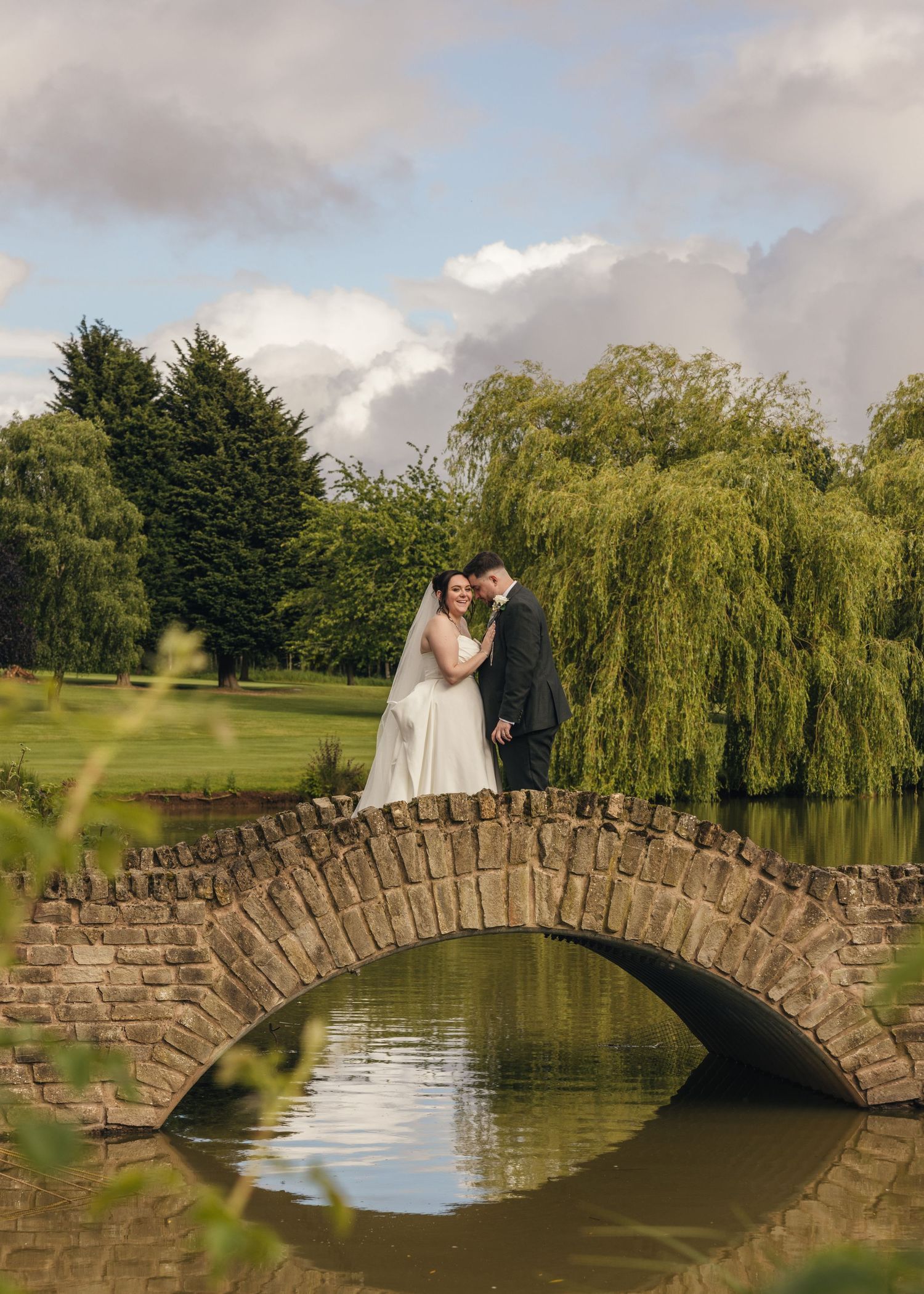Cortney and Dan standing together on a stone bridge over the lake at Windmill Village Hotel in Coventry.