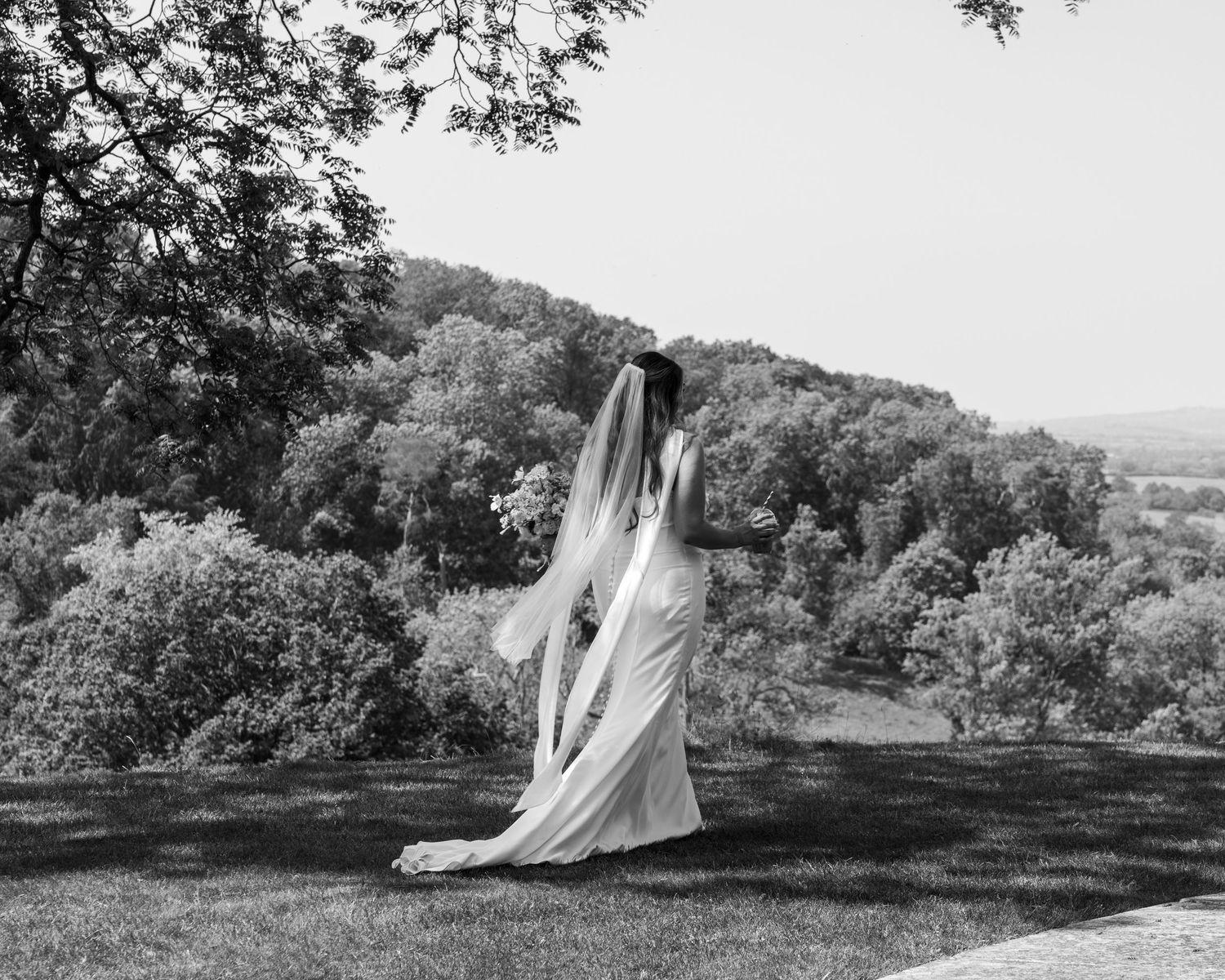 A black and white photo of a bride walking with her iced coffee to talk to her loved ones, captured by EvieSJPhotography.