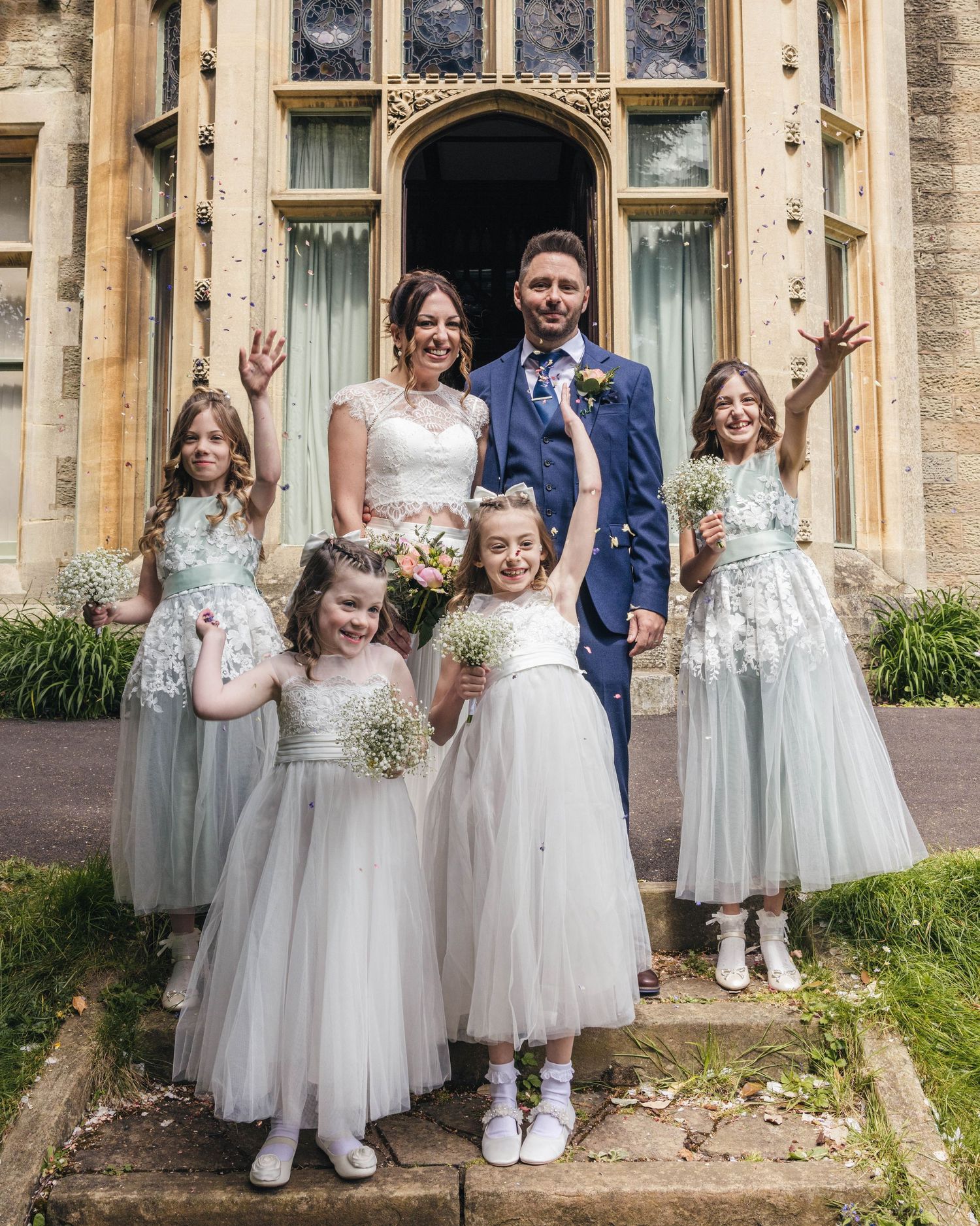 A bride, groom and their daughters having a group photo throwing confetti after the ceremony, captured by EvieSJPhotography.