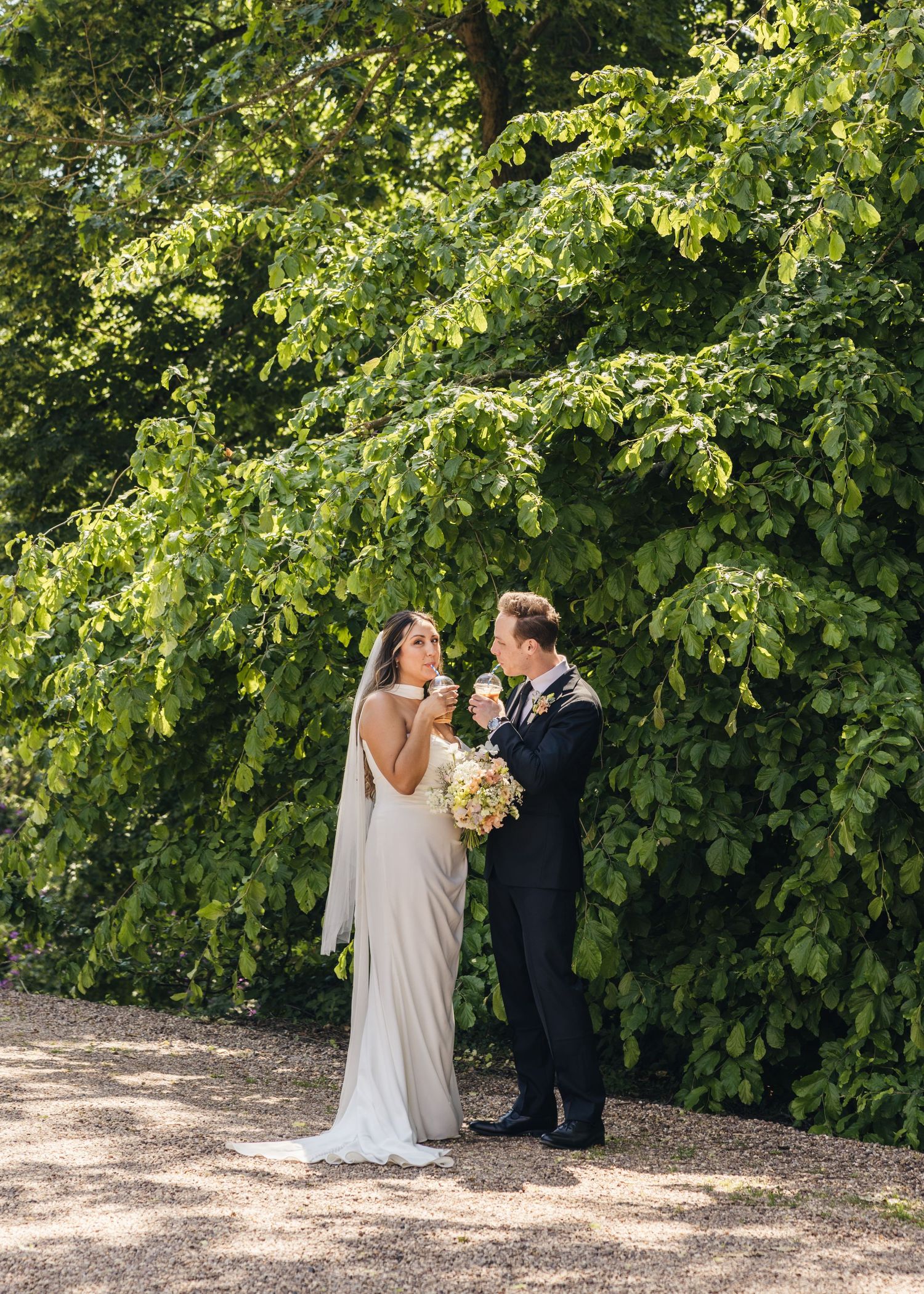 A bride and groom having a moment together, enjoying their iced coffee on their wedding day, captured by EvieSJPhotography.